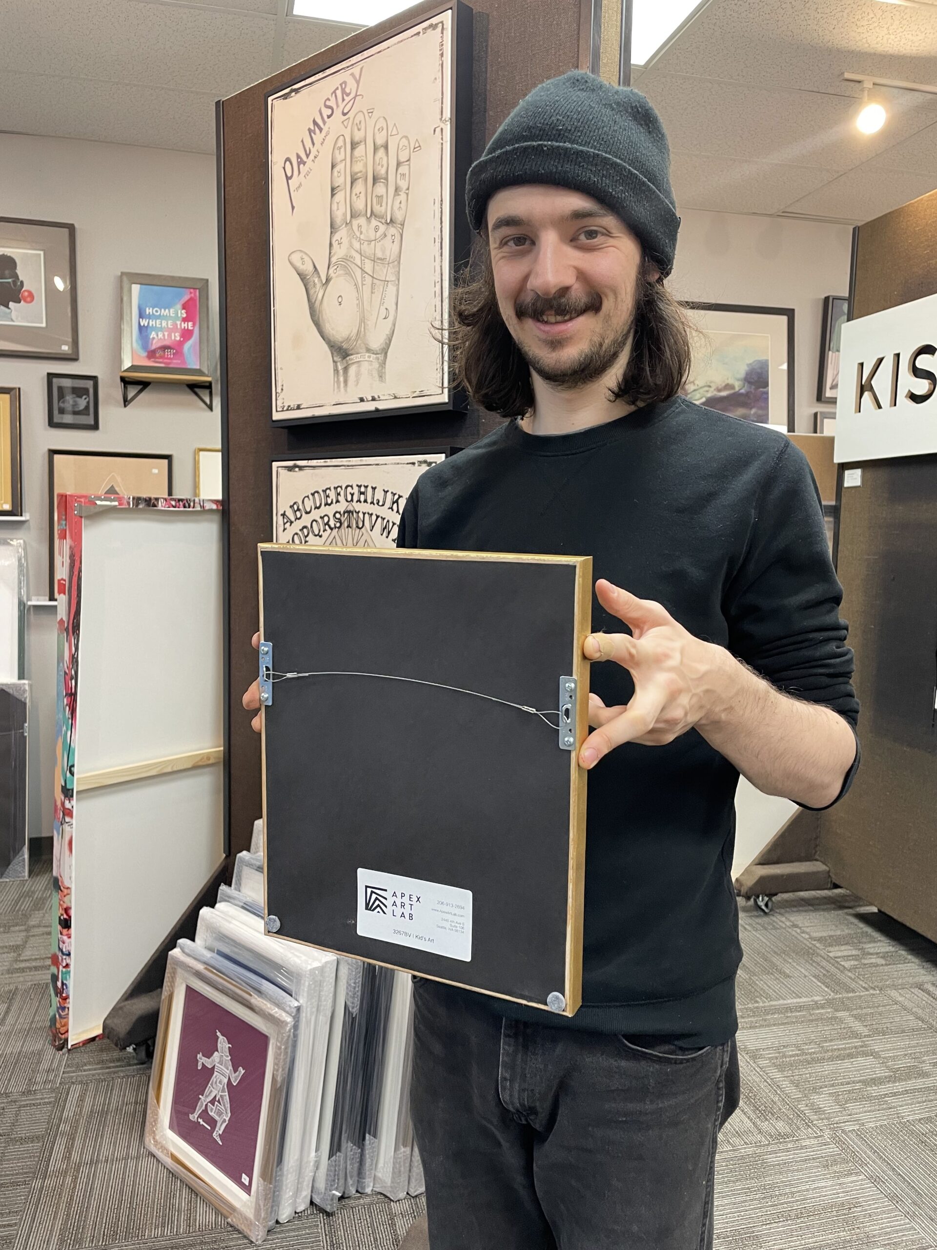 Staff member proudly holding up a completed framing project. Demonstrating the proper backing with paper, wire and bumpers